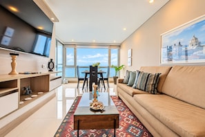 Sala de estar moderna com sofá, mesa de centro e vista para o mar.