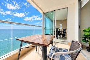 Varanda com mesa de madeira e cadeiras de vime, com vista para o mar.