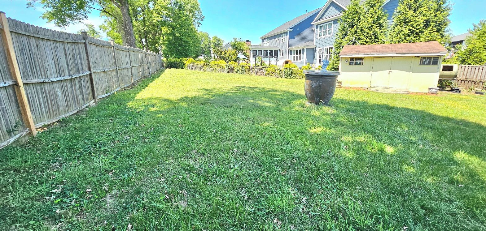 Ein Garten mit Holzzaun, einem großen Pflanzkübel und einem Haus im Hintergrund.