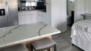 Una cucina compatta con un piano di lavoro in marmo, un frigorifero, un forno a microonde e un lavello.