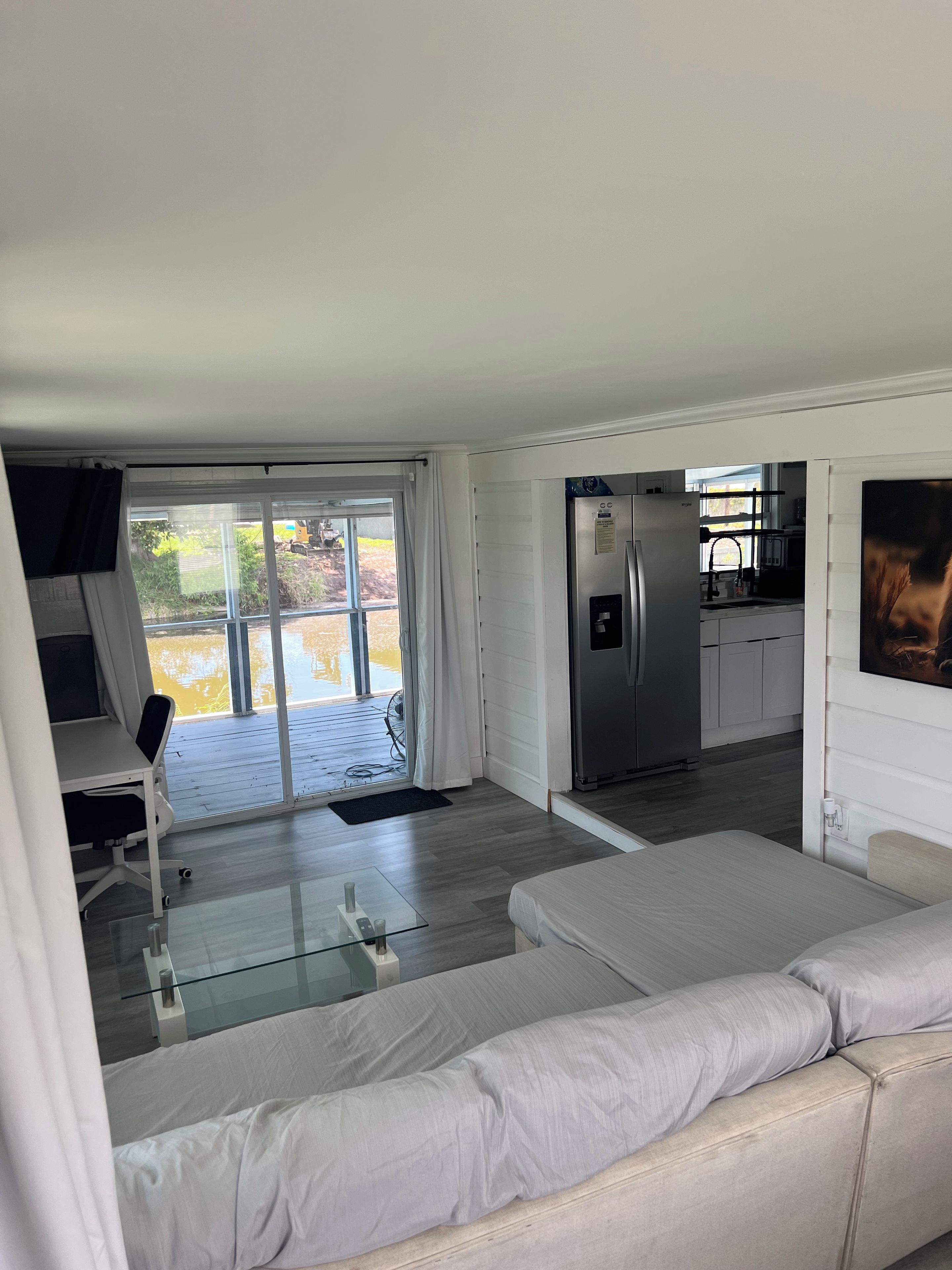 Una sala de estar moderna con un sofá, una mesa de centro de vidrio y una zona de cocina con refrigerador.