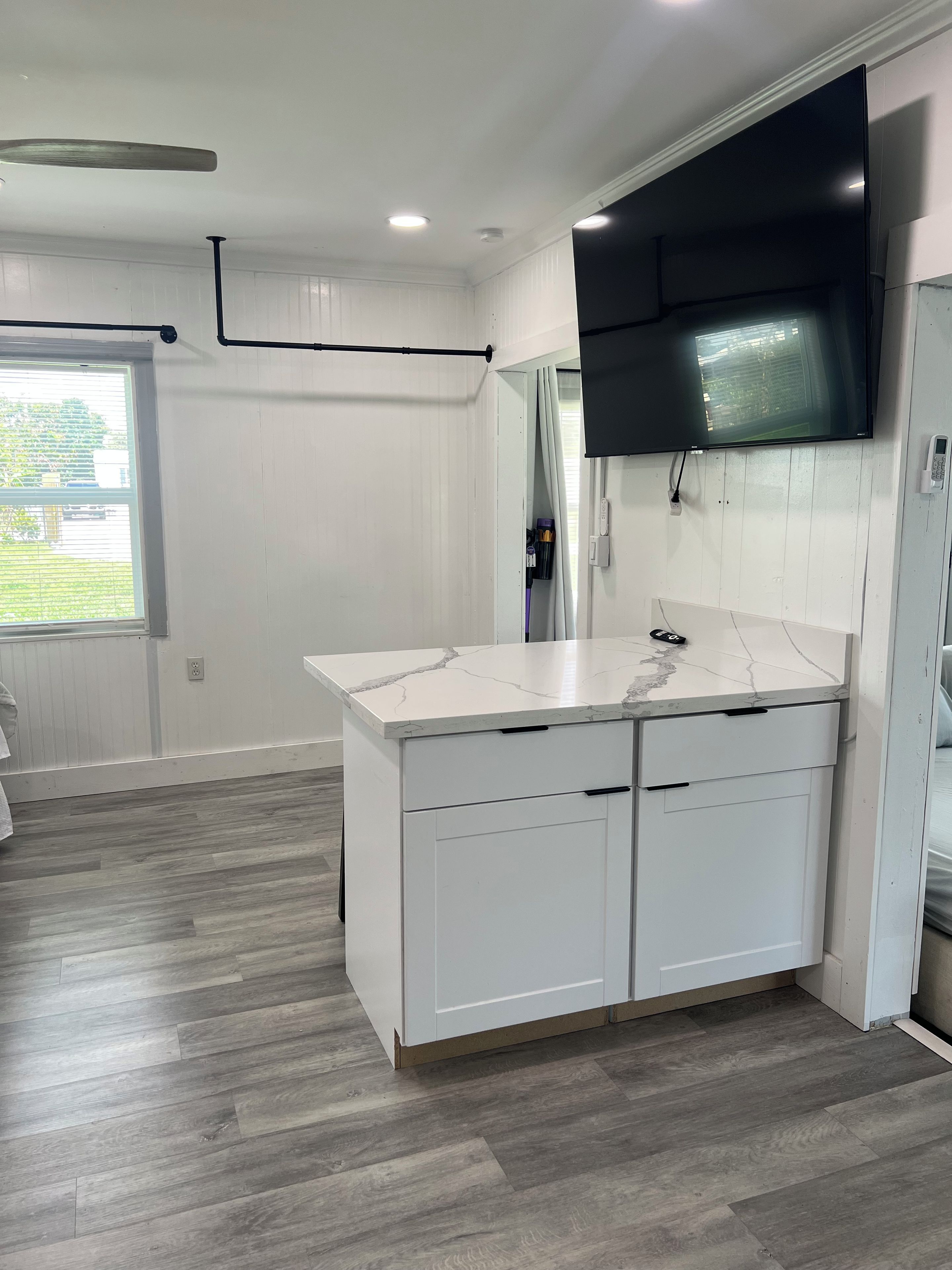 A modern kitchen with white cabinetry, a marble countertop, and a built-in TV.