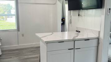 A modern kitchen with white cabinetry, a marble countertop, and a built-in TV.
