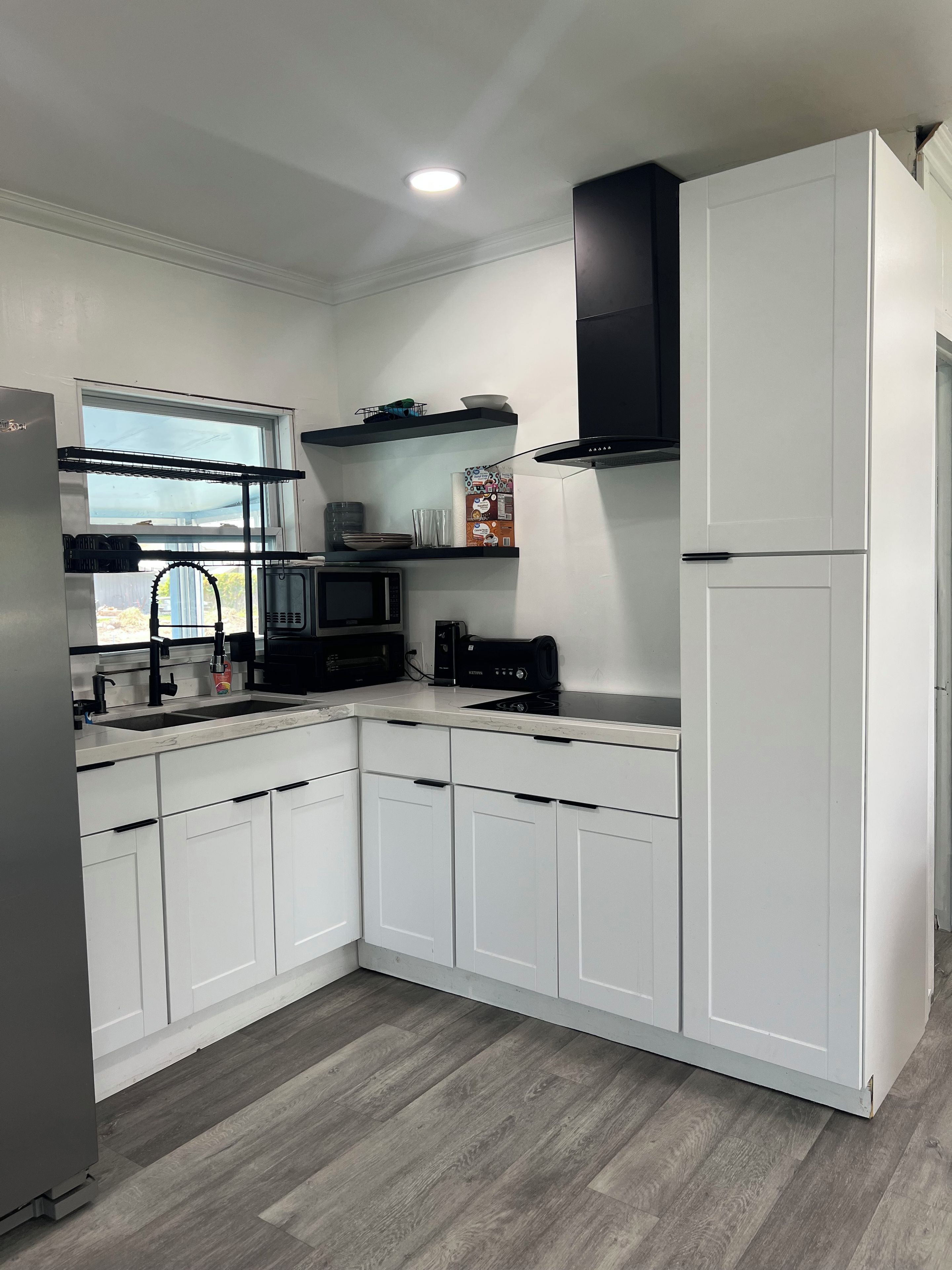 Una cocina moderna con armarios blancos, microondas, tostadora y ventana sobre el fregadero.
