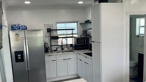 Una cucina moderna con mobili bianchi, frigorifero in acciaio inossidabile, forno a microonde e una finestra che lascia entrare luce naturale.