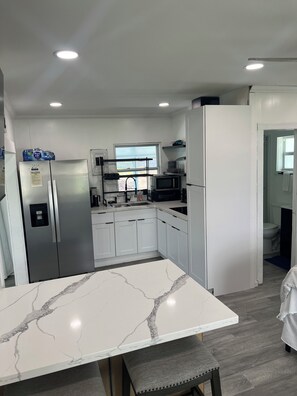 A modern kitchen with white cabinetry, a stainless steel refrigerator, a microwave, and a window providing natural light. - Waterfront home with a screened in porch (Okeechobee)