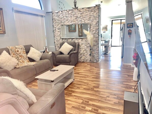 A modern living room with a stone accent wall, a sofa set, and a dining area in the background. -  Centrally located room in Glendale (Glendale)
