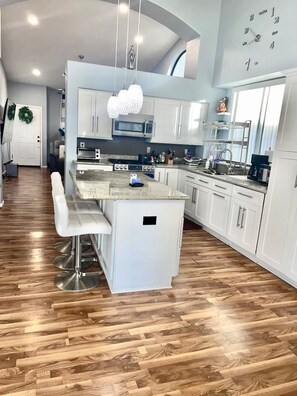 A modern kitchen with white cabinetry, a central island with bar stools, a microwave, and a coffee machine. -  Centrally located room in Glendale (Glendale)