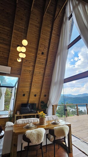 A dining area with a wooden ceiling, a table with chairs, and a view of the outdoors.
