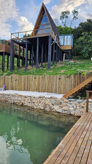 A modern house with a glass facade, wooden deck, and a small pond.