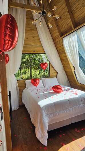 A bedroom with a wooden ceiling, a bed with white bedding, and a window with curtains.