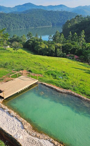 A clear view of a natural hot spring surrounded by lush greenery and hills.