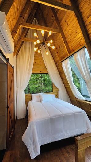 A bedroom with a wooden ceiling, a bed with white bedding, and a hanging light fixture.