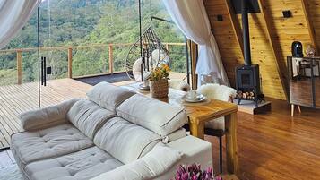 A cozy loft bedroom with a large window, a sofa, a wooden table, and a hanging chair.