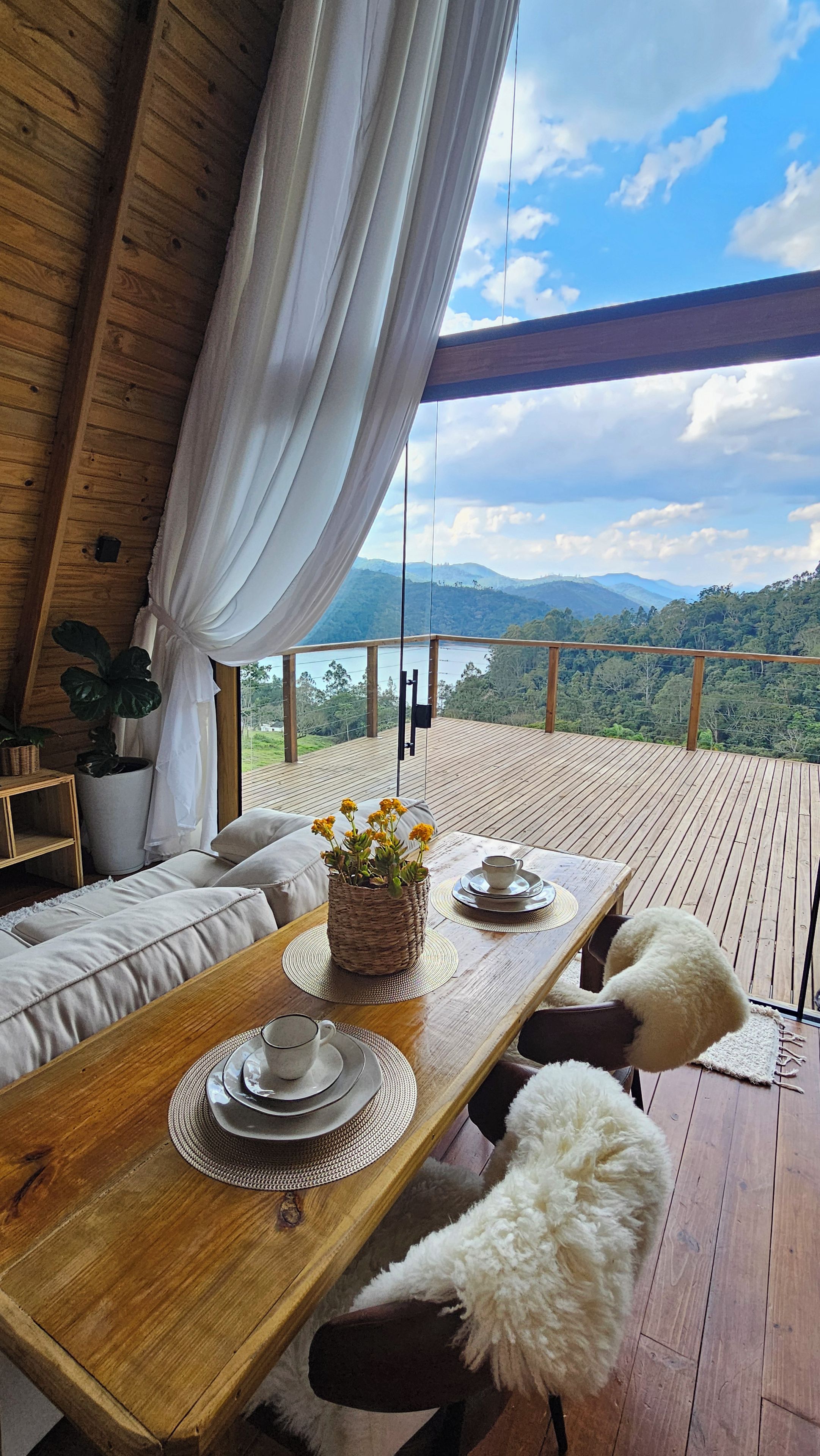 Une terrasse en bois avec une table à manger pour deux personnes, un canapé et une vue sur un paysage montagneux.