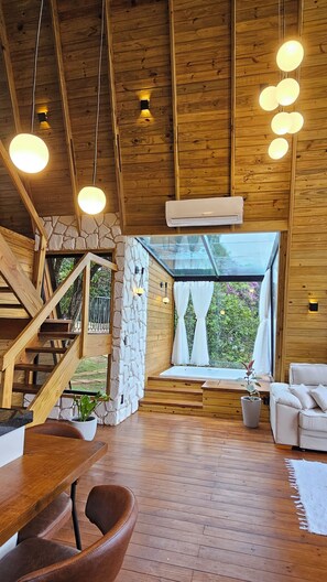 A wooden interior with a stone wall, a staircase, a glass door leading outside, and a white sofa.
