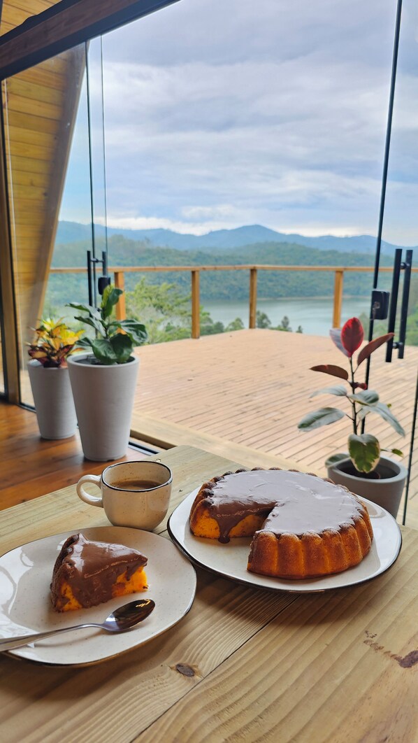 A dining table with a cake and coffee, potted plants, and a view of mountains.