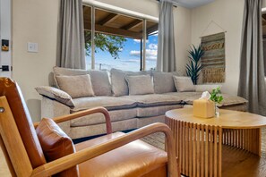 Un salon avec un canapé, une table ronde en bois et une vue sur l’extérieur.