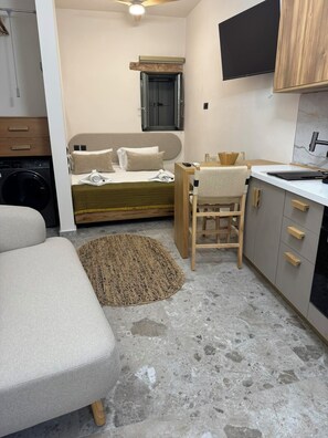 Ein kleines Hotelzimmer mit Bett, einer Küchenzeile, einem Sessel und einer Waschmaschine.