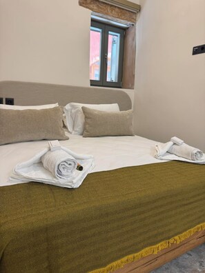 Ein Hotelzimmer mit einem Bett, Kissen, einem zusammengerollten Handtuch und einem Fenster.
