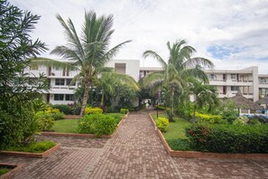 A hotel courtyard with a paved walkway, palm trees, and a pool area. - Sunsets & Serenity at Playa Escondida | 2BR Beachfront Getaway (Mazatlan)