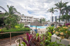 Ein Hotel mit Swimmingpool, Palmen und Reetdachschirmen.