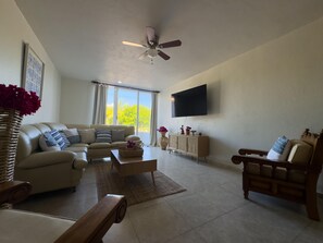 A living room with a sofa, coffee table, TV, and a ceiling fan. - Sunsets & Serenity at Playa Escondida | 2BR Beachfront Getaway (Mazatlan)