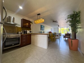 Een moderne keuken met een centraal eiland, een eethoek met tafel en stoelen, en een grote kamerplant.
