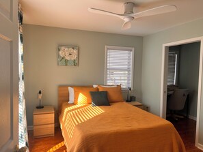 A bedroom with a bed, a nightstand, a lamp, a ceiling fan, a window with blinds, and a door leading to another room. - New listing discount! Sunny Shores on Hartwell- Dock, kayaks, pedal boat, games (Martin)
