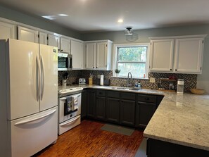 A kitchen with white cabinets, a stainless steel refrigerator, a microwave, a sink, and a window providing natural light. - New listing discount! Sunny Shores on Hartwell- Dock, kayaks, pedal boat, games (Martin)