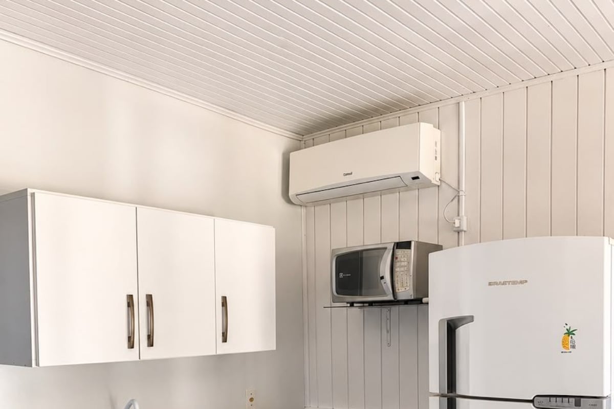 Une cuisine compacte avec des meubles blancs, un four à micro-ondes encastré, une cuisinière à gaz et un réfrigérateur blanc.