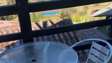 Un balcón con una mesa de vidrio y sillas de metal, con vistas a una zona residencial con casas y vegetación.