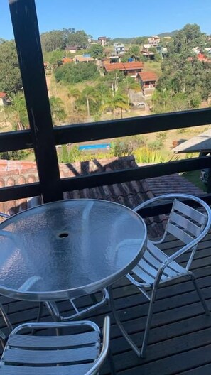A balcony with a glass table and metal chairs, overlooking a residential area with houses and greenery. - Pousada Cristais do Rosa (Imbituba)