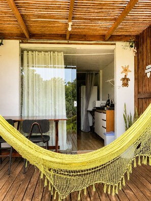 Una habitación con techo de madera, una hamaca, una mesa de comedor y una zona de cocina visible a través de una puerta abierta.