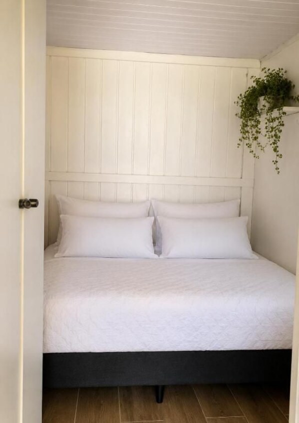 Una cama con ropa blanca, una estructura de color oscuro y un cabecero blanco.
