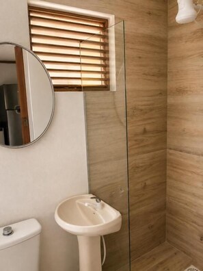 A bathroom with a wooden wall, a glass shower enclosure, a white sink, and a toilet. - Pousada Cristais do Rosa (Imbituba)