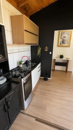 Una cocina con estufa, pileta y alacenas, un respingo de azulejos blanco y negro, y techo de madera.