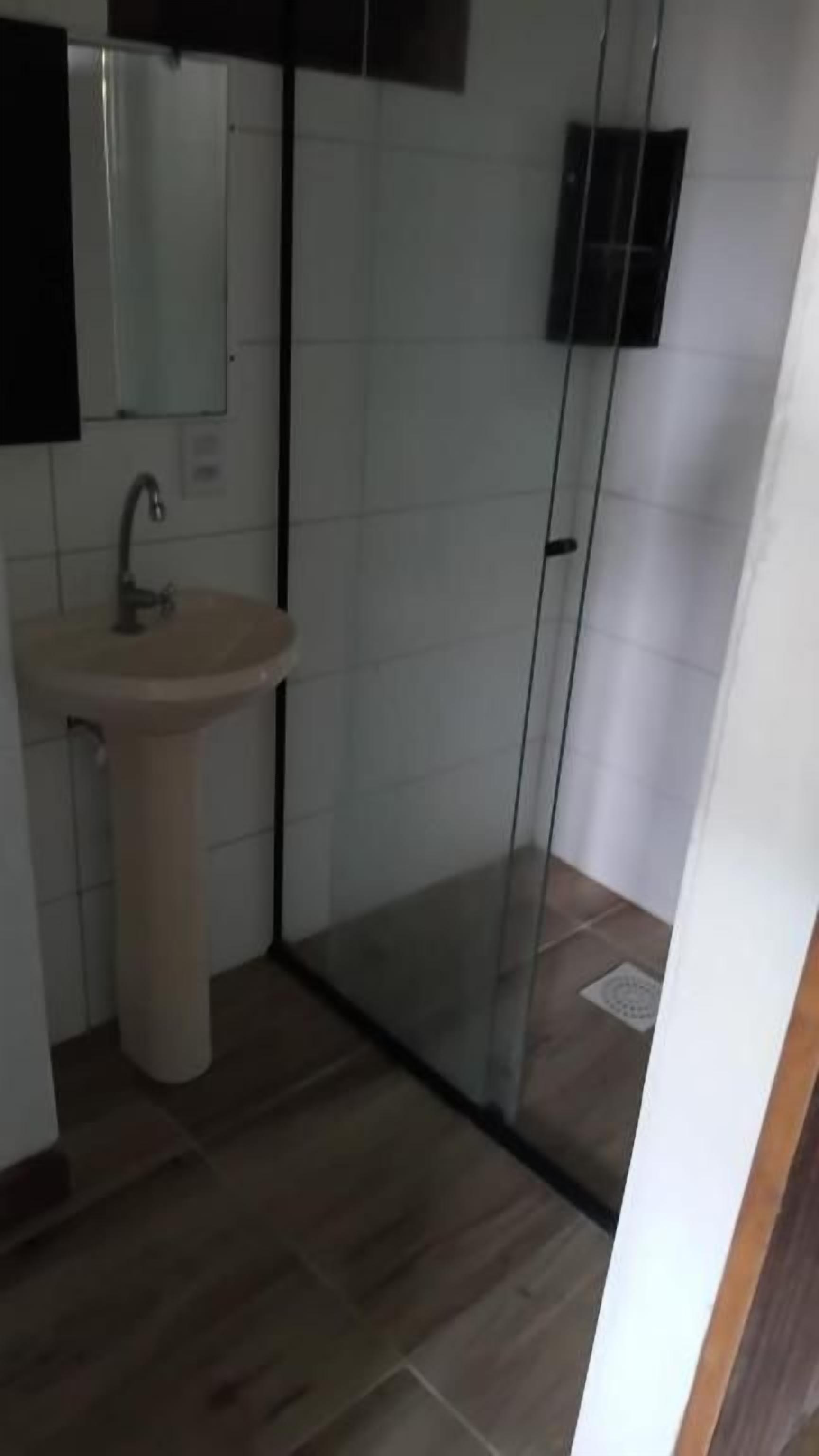 Casa de banho com chuveiro em cabine de vidro, lavatório e espelho.