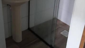 Casa de banho com chuveiro em cabine de vidro, lavatório e espelho.