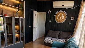 A modern living room with a teal sofa, wooden flooring, a hanging light fixture, and a wall-mounted air conditioning unit. - Pousada Cristais do Rosa (Imbituba)