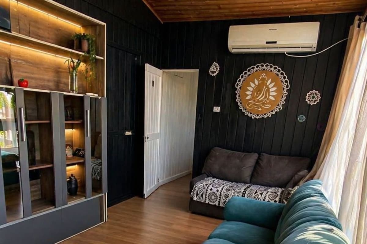 Un salon moderne avec un canapé de couleur turquoise, un plancher en bois, un luminaire suspendu et un climatiseur fixé au mur.