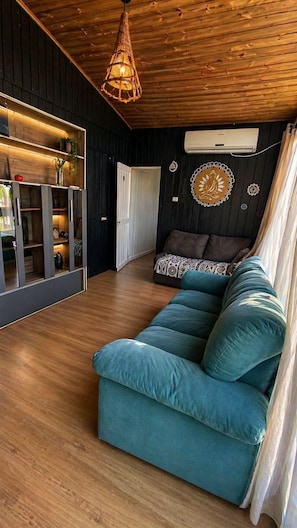 Un salon moderne avec un canapé de couleur turquoise, un plancher en bois, un luminaire suspendu et un climatiseur fixé au mur.