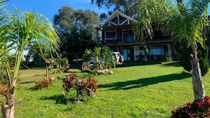 A house with a large lawn, a tree, and a car parked in front. - Pousada Cristais do Rosa (Imbituba)