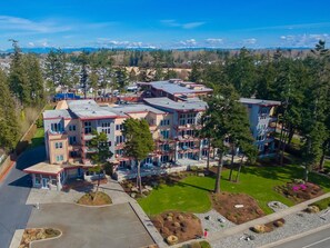 A multi-story residential building with a central courtyard, surrounded by trees and a clear view of the mountains in the distance. - GB  102: Beautiful water view! Great Birch Bay location, free Wi-Fi. (Birch Bay)