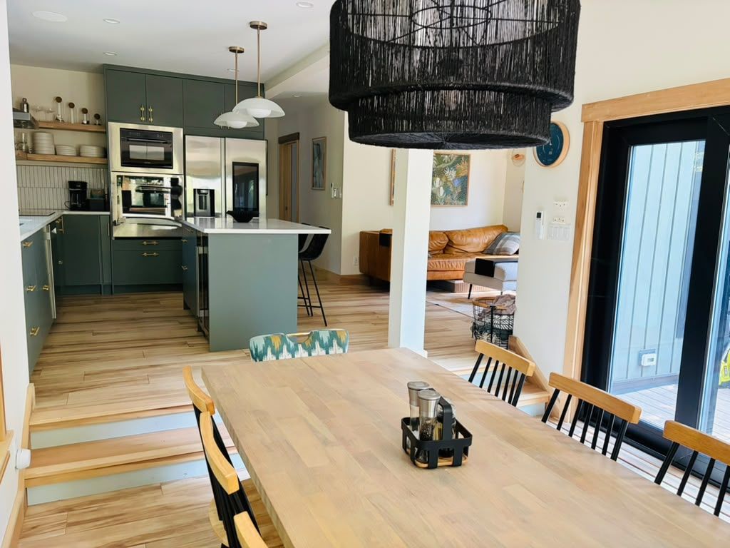 A modern kitchen with a central island, wooden dining table, and chairs.