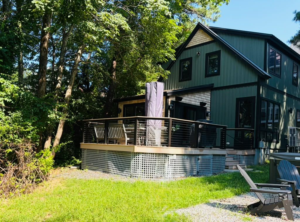 A two-story house with a deck, surrounded by trees.