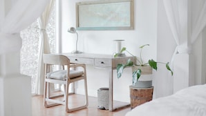Quarto com cama, escrivaninha, cadeira, abajur e planta.