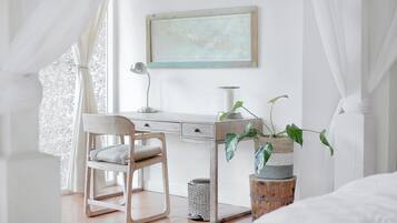 A bedroom with a bed, a desk, a chair, a lamp, and a plant.