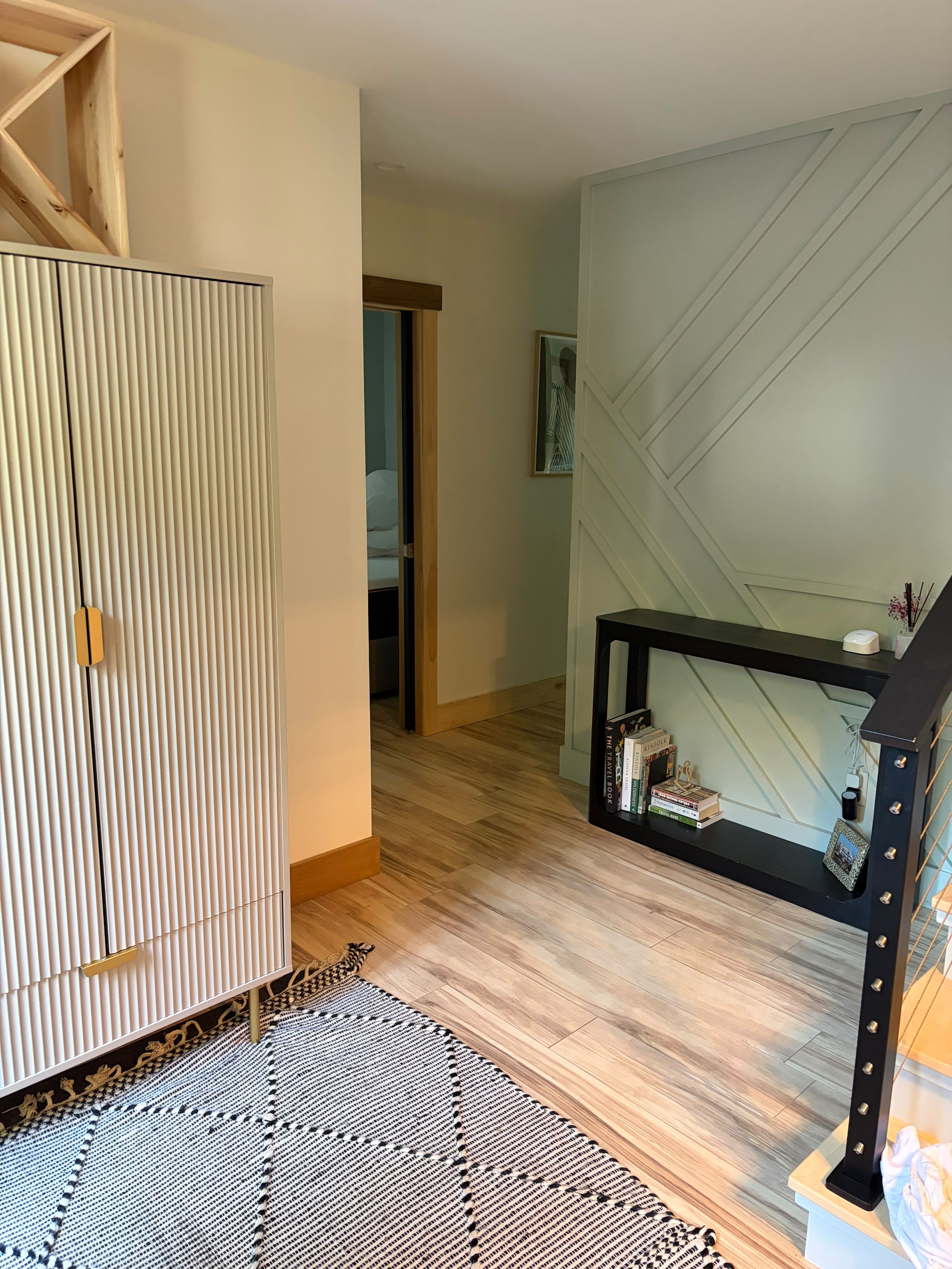 A room with a wardrobe, a console table with books, a patterned rug, and a hallway leading to another room.