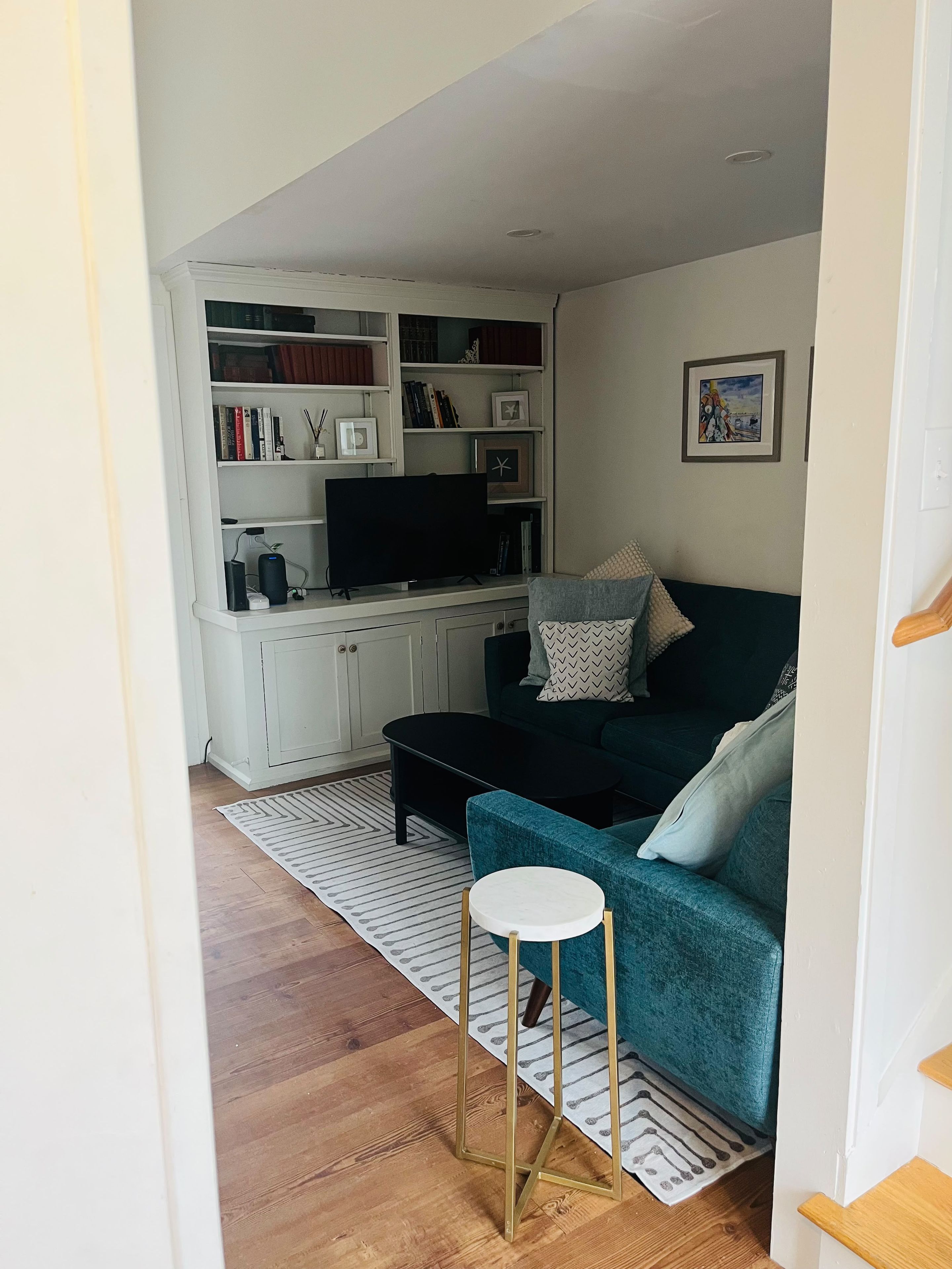 A living room with a teal sofa, a black coffee table, a white side table, and a wooden floor.